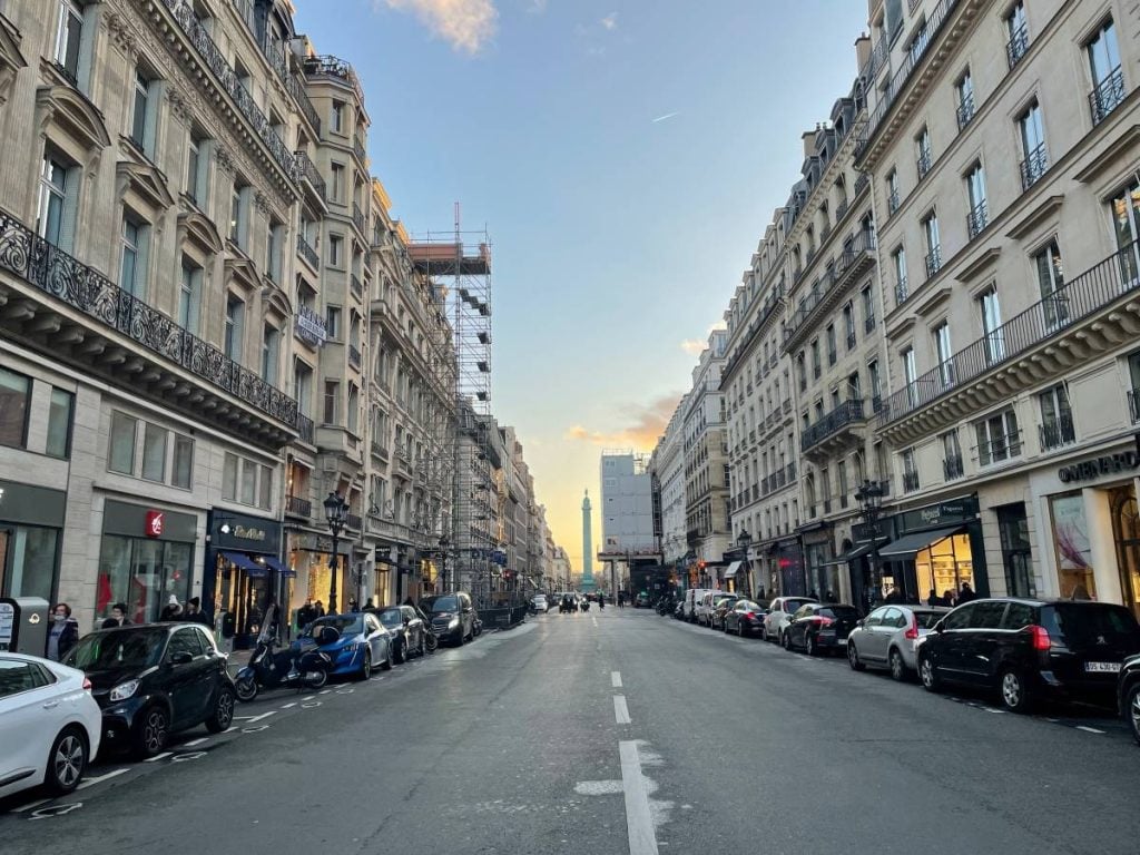 An empty Parisian street with cars parked along both sides. In the distance you can see the beginning of a sunset