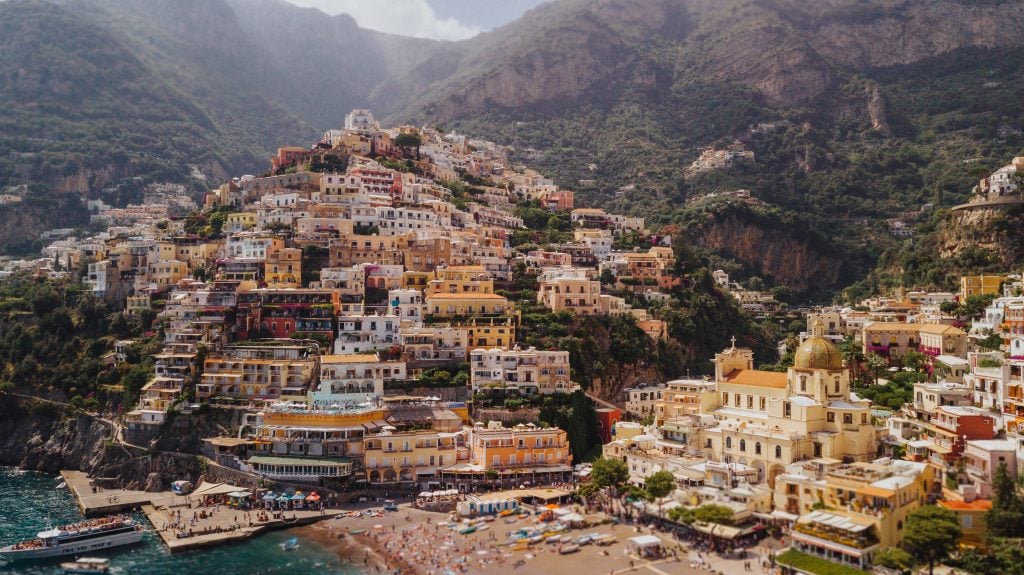 Positano, Italy: a sun-drenched coastal town amidst a mountainous coast. Layers and layers of buildings climb the mountain, all in warm shades.