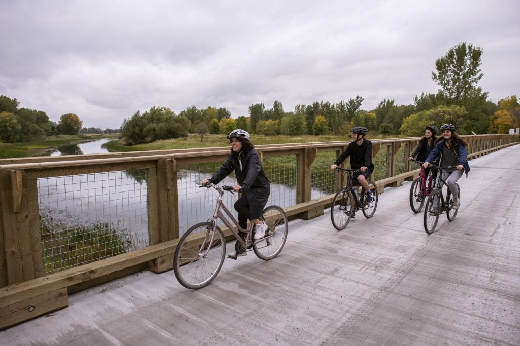 A group of cyclists riding down a wooden pathway over a river in a Quebec national park.