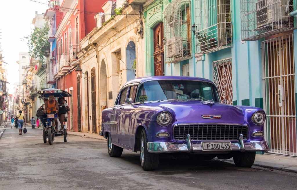 A purple classic Cadillac parked on a street of colorful buildings.