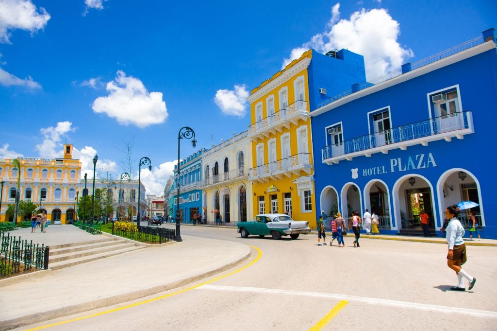 A plaza with several bright yellow and blue buildings in front of a small park.