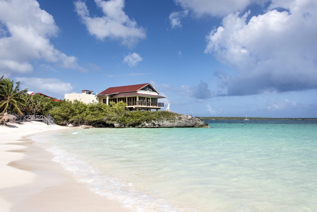 A white sand beach with crystal clear blue water and a building in the background