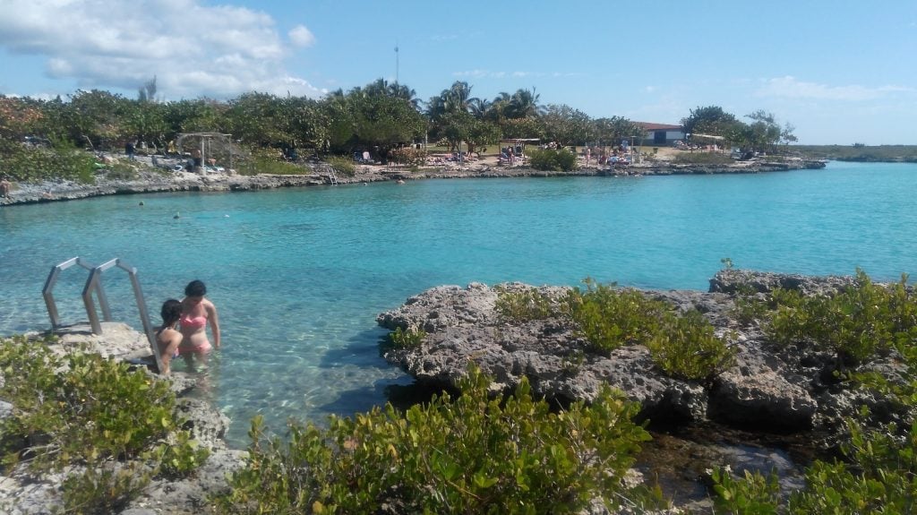 Bright blue water surrounded by grass covered rocks