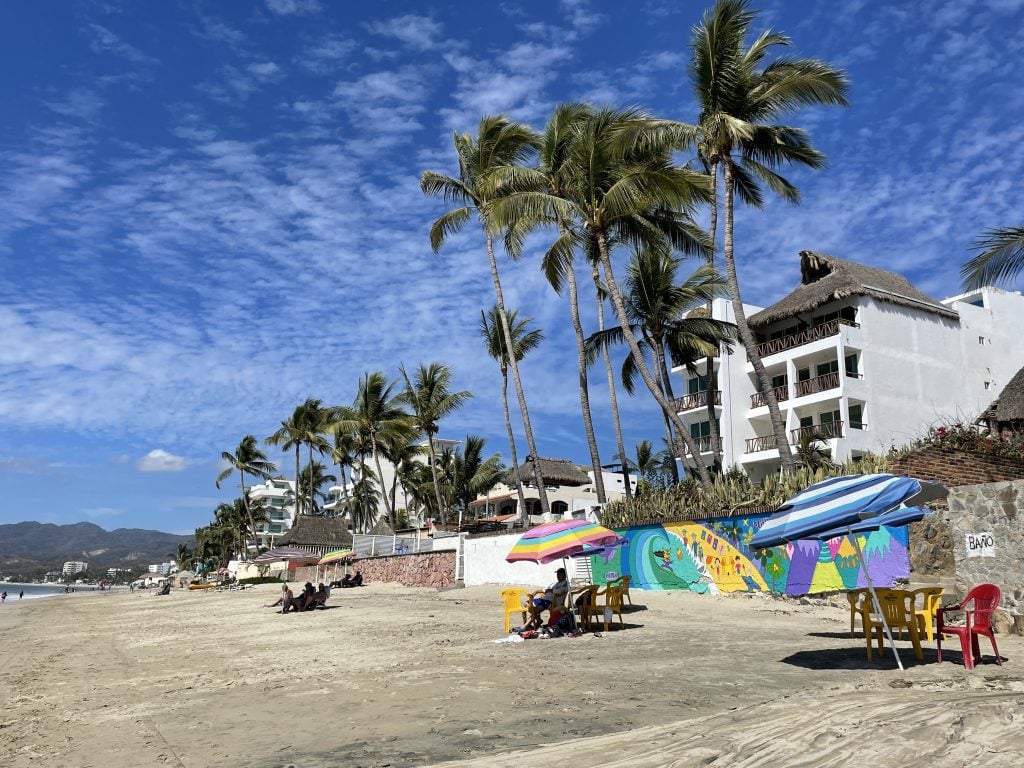 A beach backing up to white condo buildings with balconies and lots of palm trees.