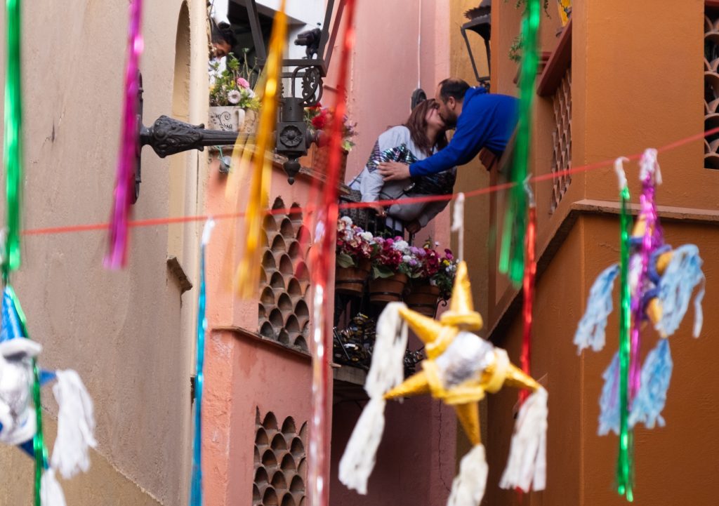A couple kissing across the balconies, hanging decorations surrounding them.
