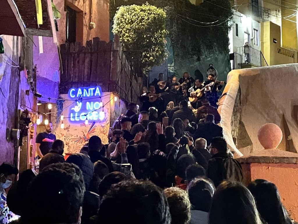 Crowds of people standing on a narrow staircase in the dark as musicians play at the top.