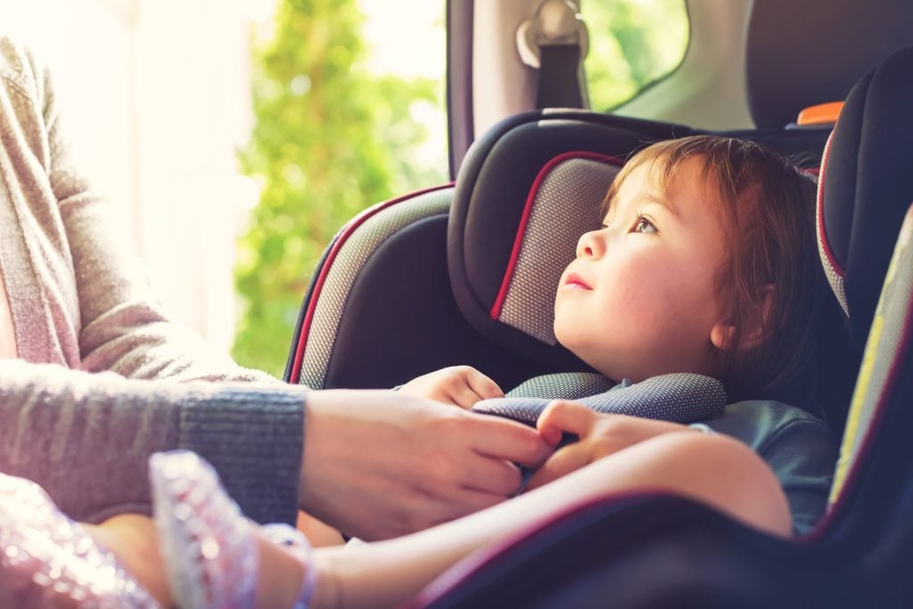 A toddler girl buckled into a car seat.