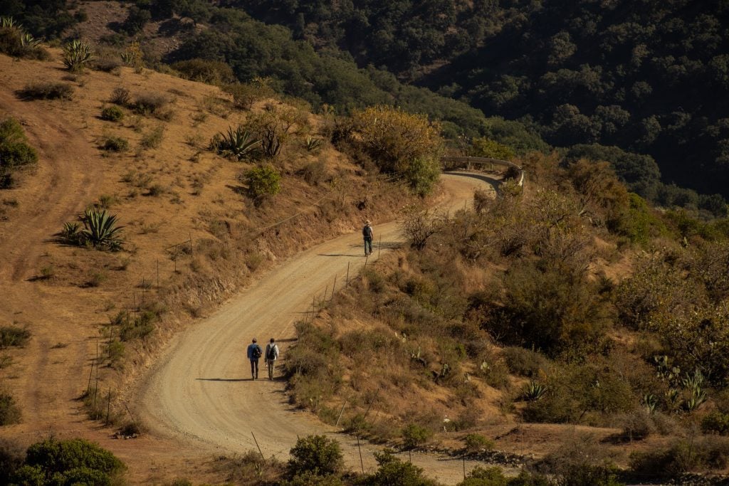 Several people walking up a curvy dirt road in the mountains.