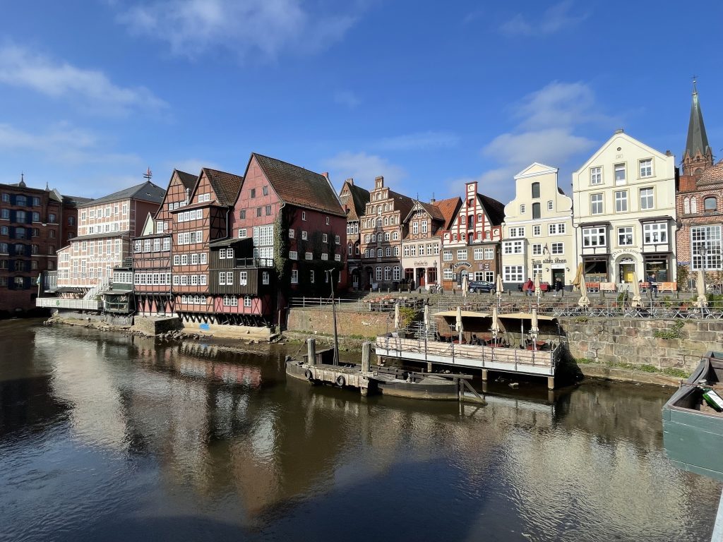 A river flowing through Luneburg, Germany, with interesting crenellated buildings and outdoor cafes along the riverside.