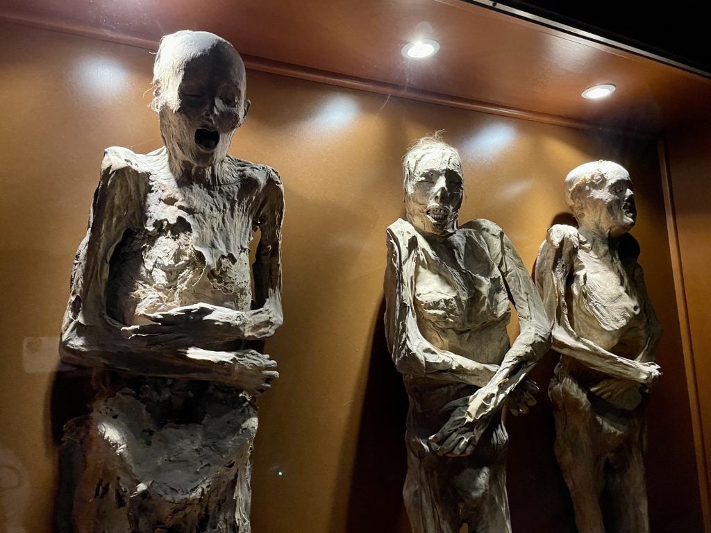 Three grotesque mummies -- human bodies mid-decomposition, their faces writhing in terror.