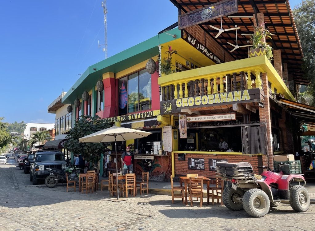 A cobblestone street in Sayulita lined with colorful shops and restaurants, including Chocobanana, the frozen chocolate banana place.