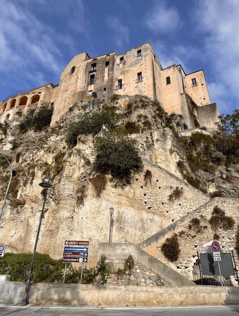 A view of stairs cut into the stone cliff and zig-zagging up the wall until they hit the stone buildings of Tropea.