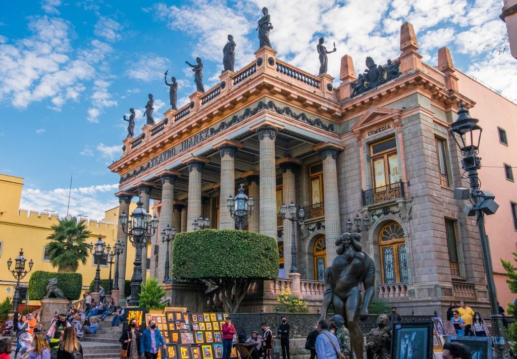 The Teatro Juarez, topped with Greek statues and featuring classical columns. Lots of people sitting in front of the steps.