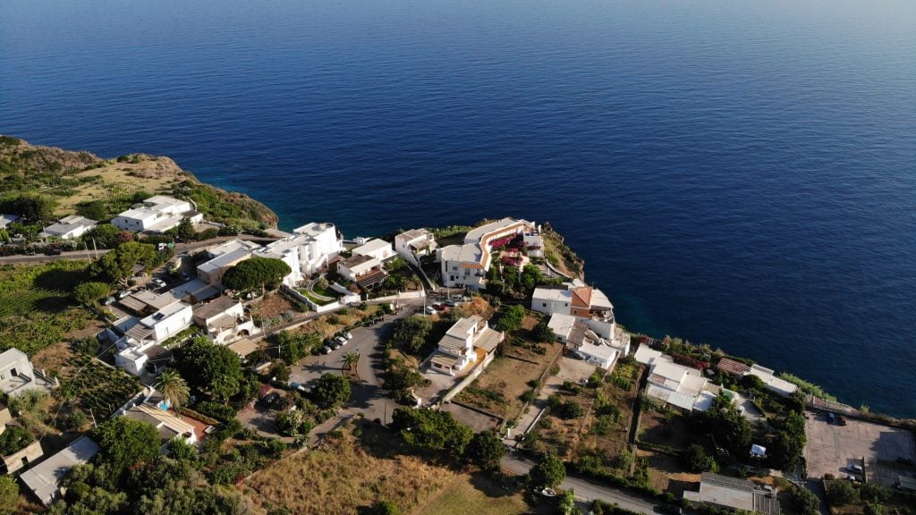 An aerial view of Tropea's coastline, bright white buildings and vineyard next to the cliffs plunging into the sea.