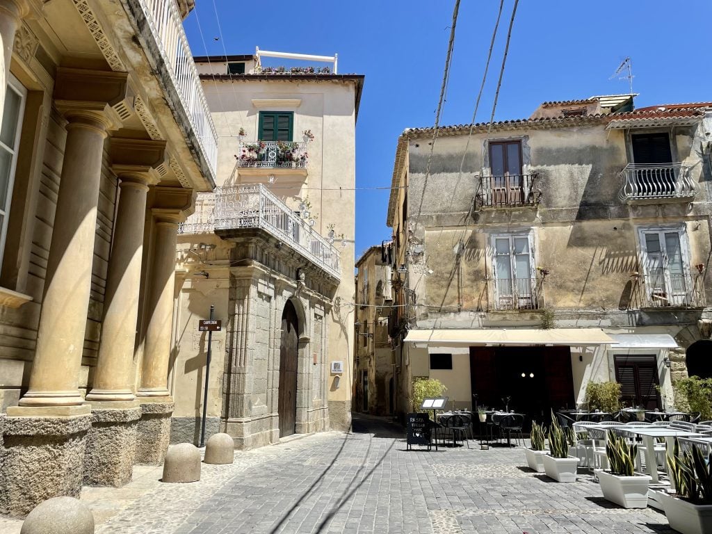 A small, quiet courtyard of tan stone buildings and some restaurants.