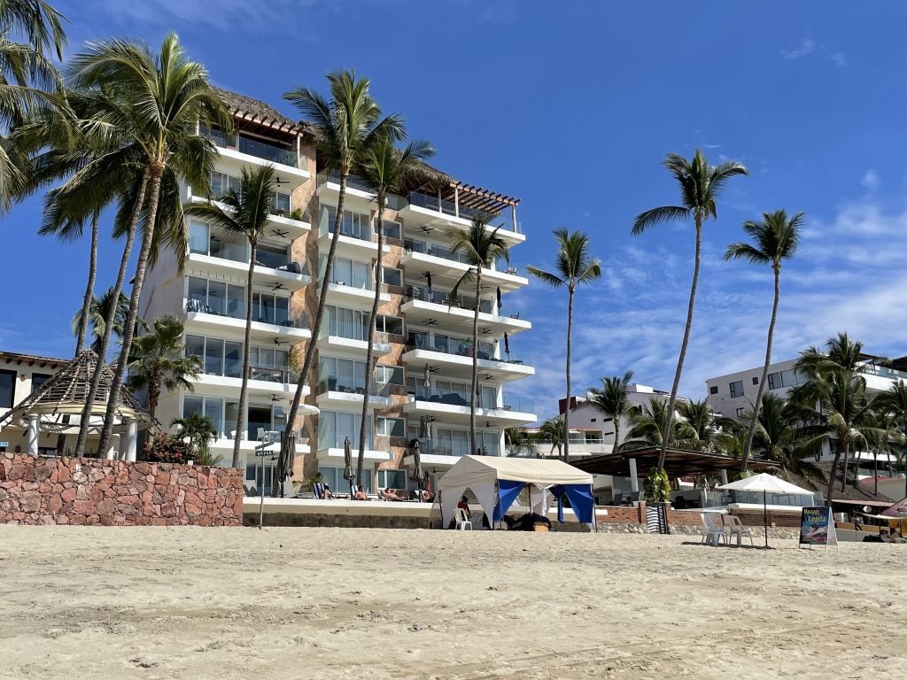 A white condo building with lots of glass balconies overlooking the beach and a massage shack.