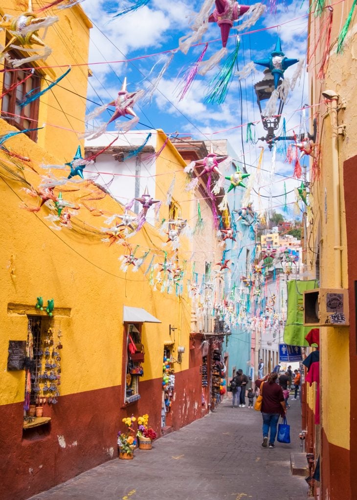 A colorful yellow and red street with foil and paper star-shaped decorations hanging across from above.