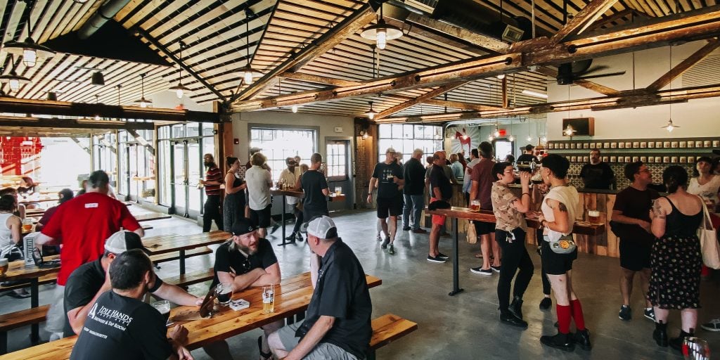 People hanging out in a brewery, some standing and some sitting at tables