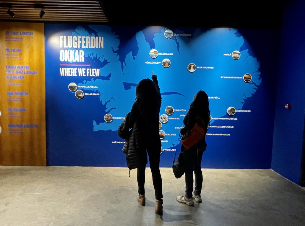 Two women standing in front of a map of Iceland reading "Where we flew" with circle-shaped photos pointing out the filming locations.