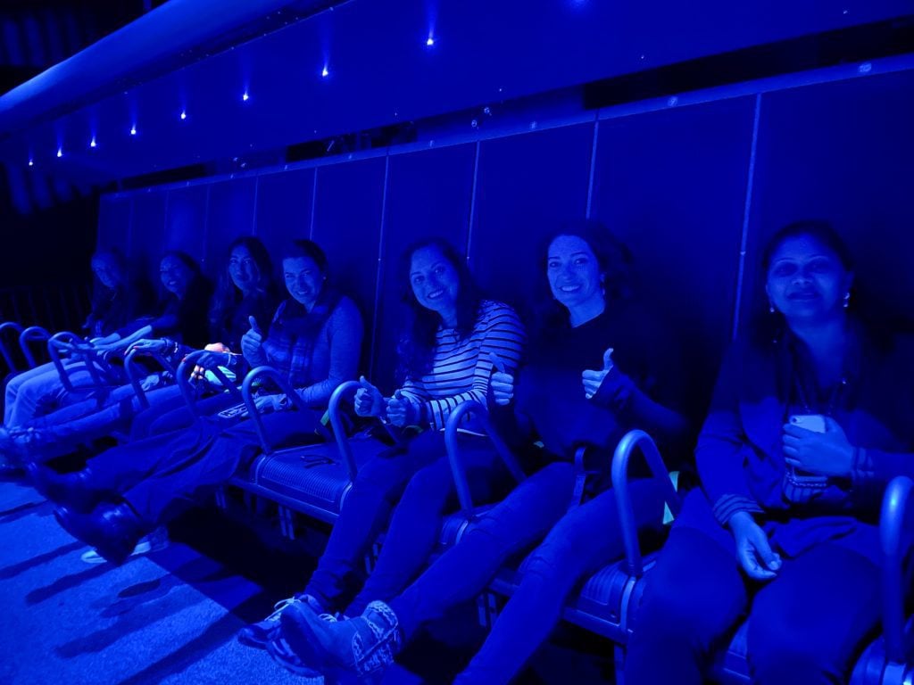 A group of girls strapped into the ride at FlyOver Iceland, giving thumbs up to the camera.