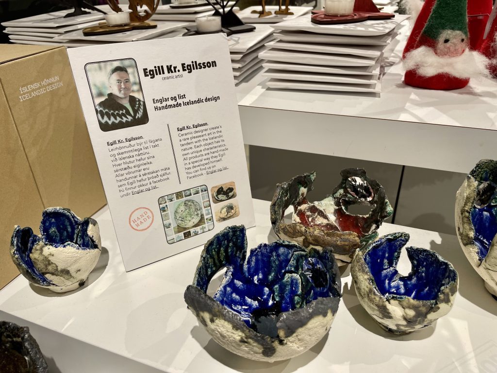 A table covered with lava sculptures that look like broken eggshells. The outside is white and the interior is glazed blue, teal, and red with shiny paint.