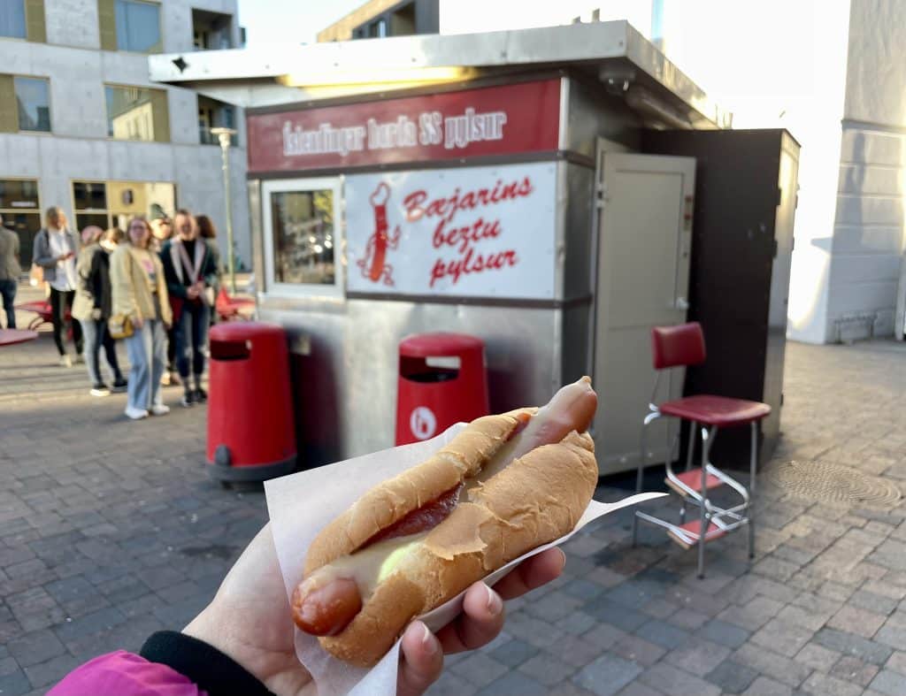 Kate holding a hot dog in front of a tiny Icelandic hot dog stand.