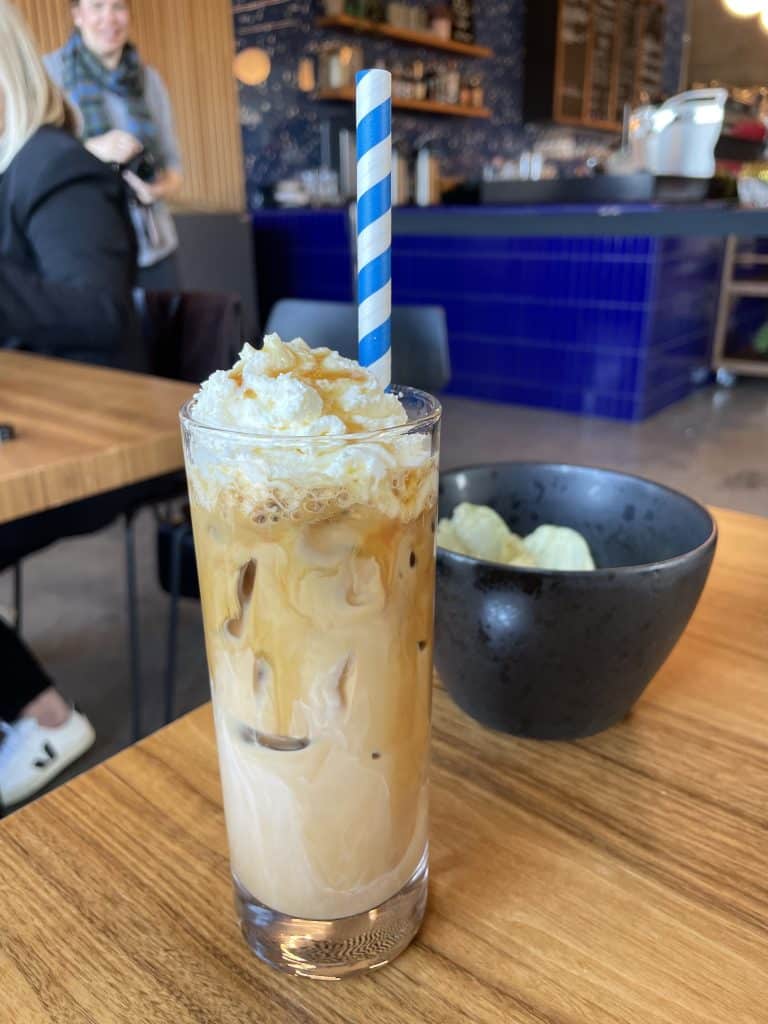 A tall skinny iced latte topped with whipped cream, caramel, and a striped straw.