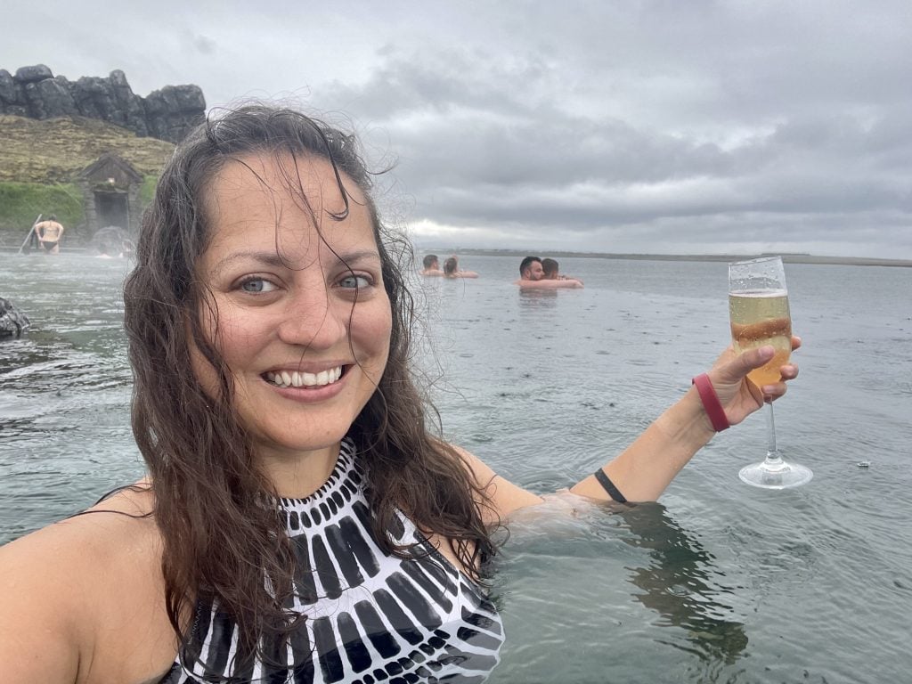 Kate swimming in the Sky Lagoon, holding a glass of champagne. It's raining and her hair is starting to stick against her face.