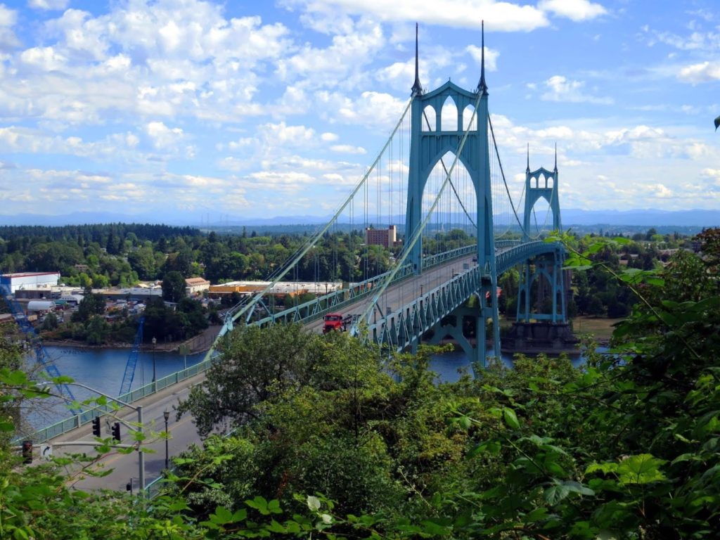 A tall green suspension bridge connecting two wooded sides of a river.