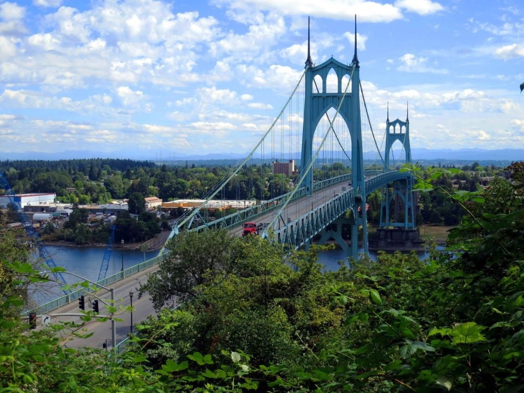 A view of St Johns Bridge in Portland, with lots of green trees in the foreground and bleu skies behind