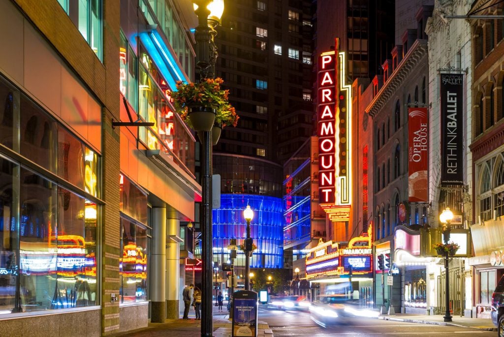 Boston's theater district, including the famous Paramount Theater, lit up in neon colors at night.