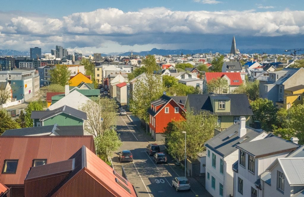 The view above Reykjavik: lots of colorful metal-sided houses with trees, the pointy church in the distance, and mountains further behind it.