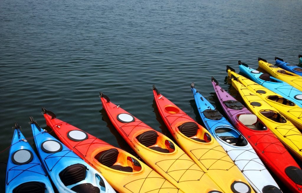 A row of brightly colored kayaks against dark blue water.