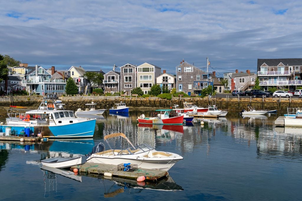 Several boats in a calm harbor and several beach homes on the shore.