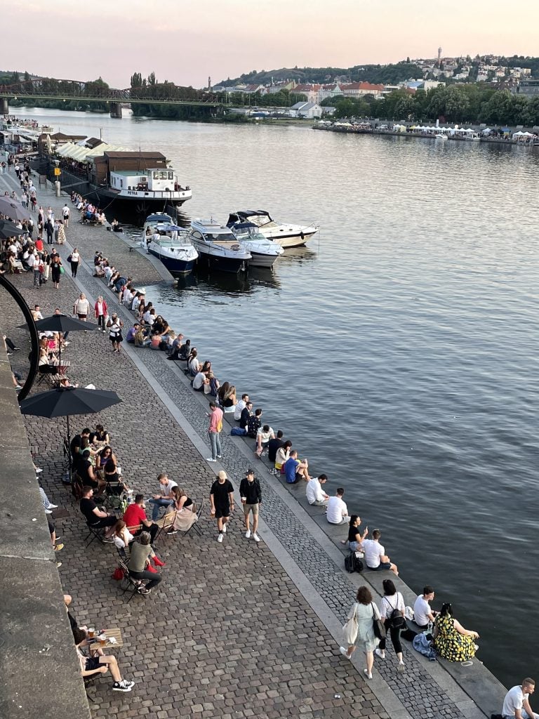 People sitting on the shore of the river in Prague just before sunset, the light delicate and gray-pink.