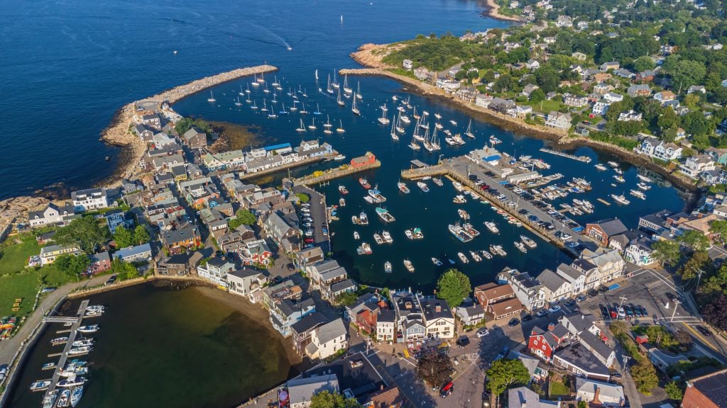 An aerial shot of Rockport with the buildings on BearSkin Neck huddled together, and lots of boats in the harbor.