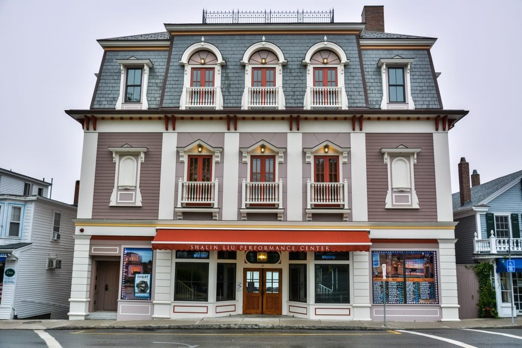 A modern Victorian-style building that looks more like a mansion than a theater, with windows with balconies, painted shades of mauve, cream, and navy blue. It reads Shalin Liu Performance Center on a red awning.