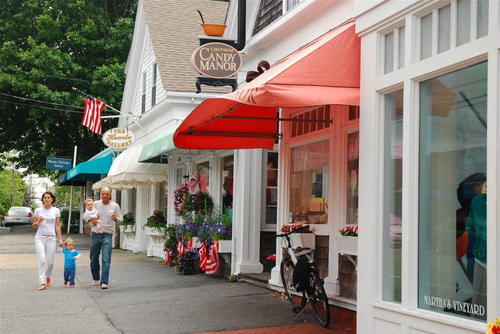 A man and woman with two toddlers walking down the street past Chatham Candy Manor and two galleries.