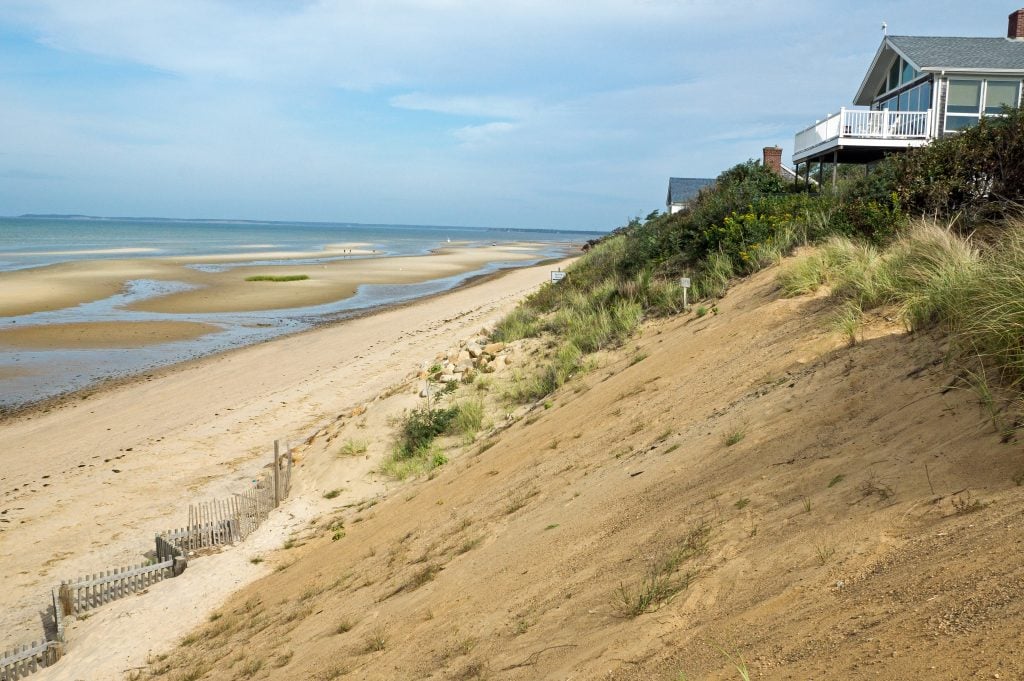 A house built on a steep hill of sand leading down to a peaceful beach.