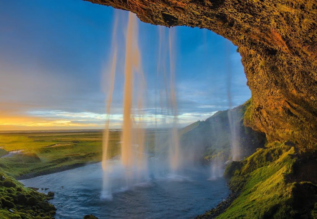 A waterfall falling so gently it looks like sand, behind a green mossy cliff.