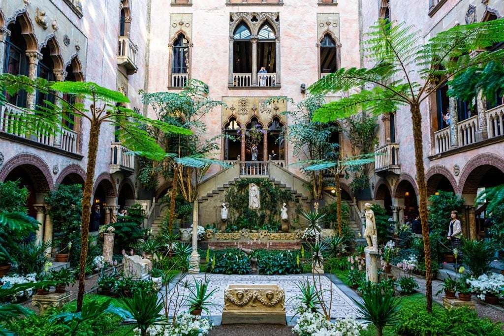 A sand-colored stone museum courtyard filled with pointy Gothic windows, statues, and so much lush greenery.
