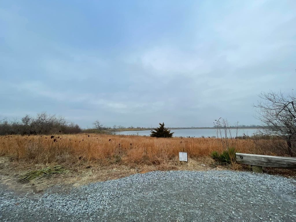 A gravel parking lot with green and water in the distance