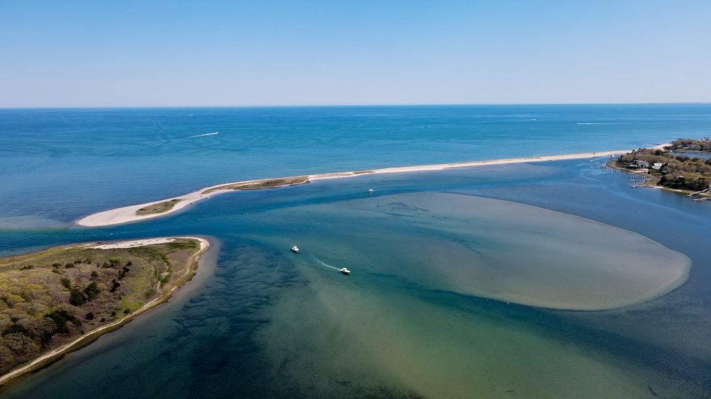 A calm green-blue harbor, a long skinny sand island stretching across and penning it in.