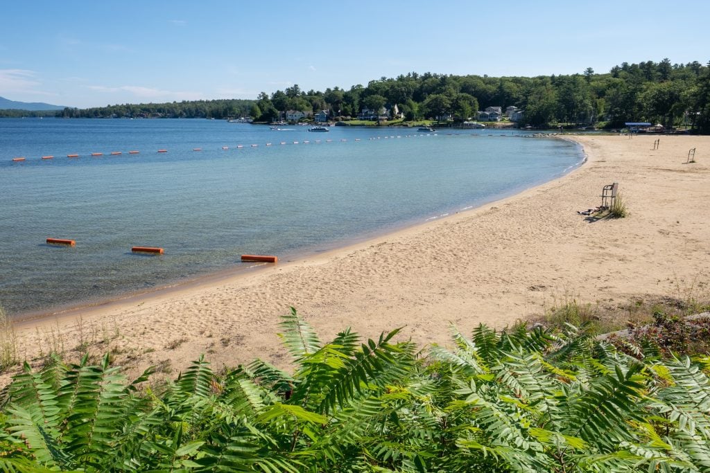 A long-super-calm brown sandy beach in front of smooth blue-green water.