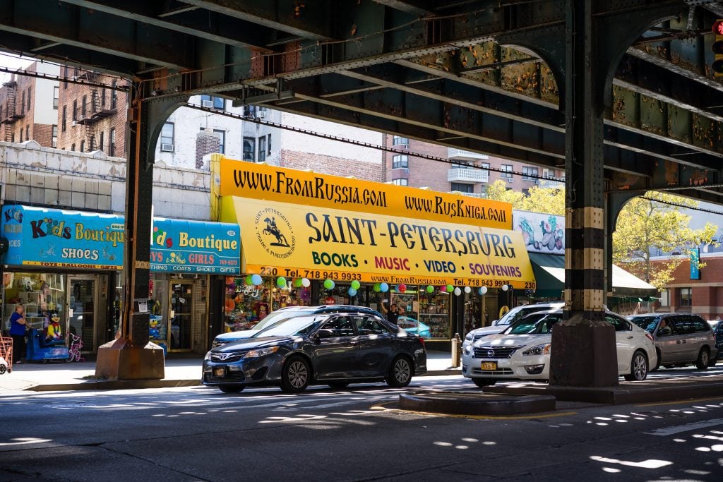 A view of a yellow sign outside a building from under an over pass with cars passing