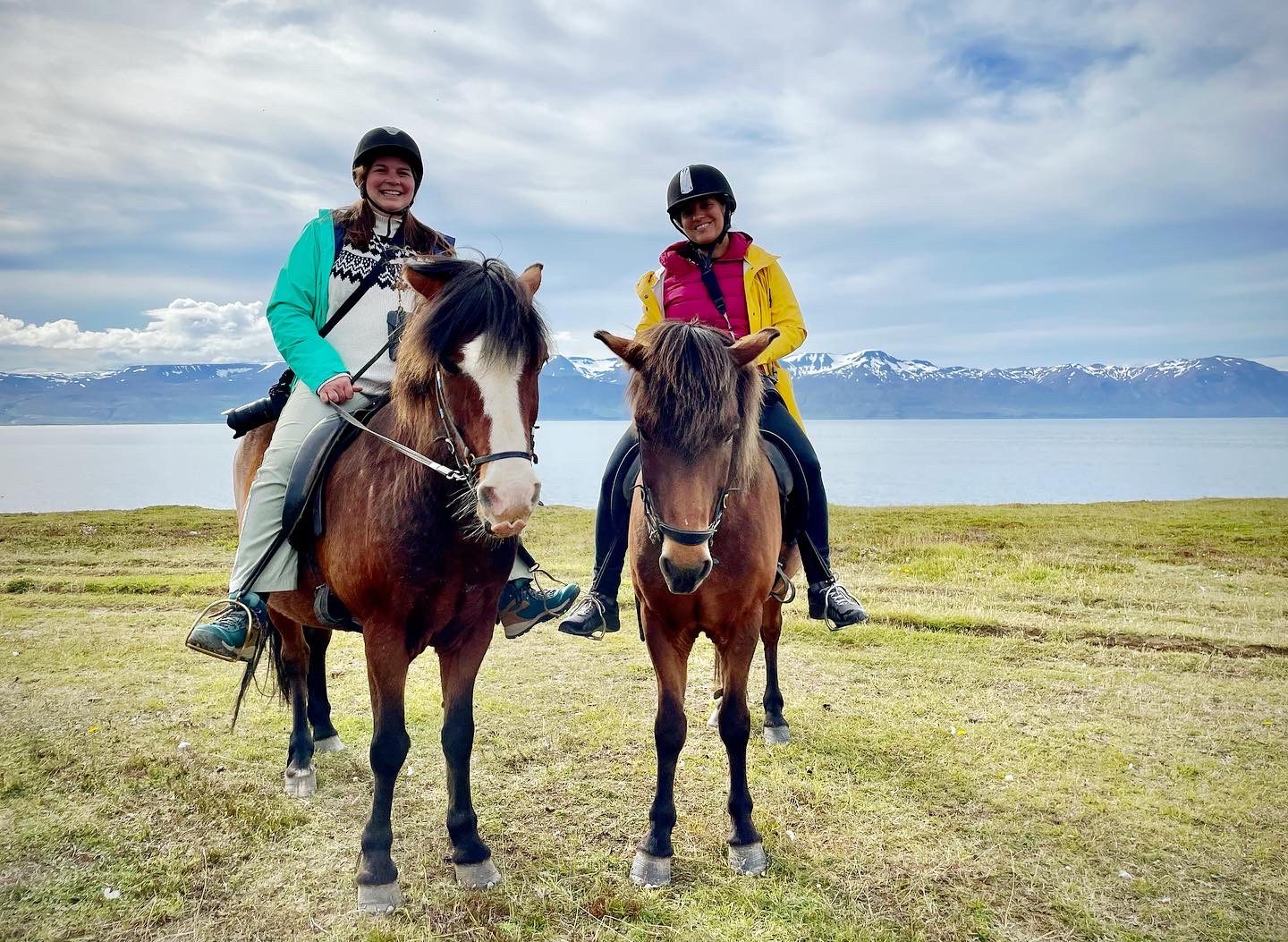 Amanda and Kate side by side on horseback in front of snow-covered mountains.