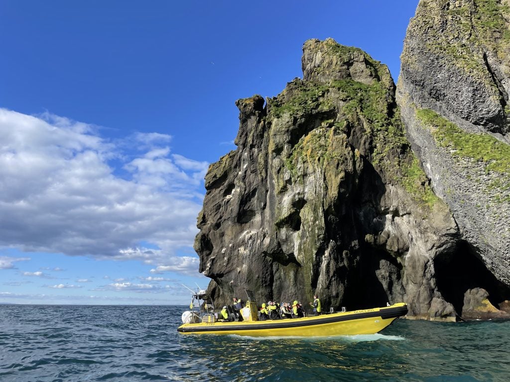 A bright yellow speedboat along the craggy cave-covered coast on a sunny day.