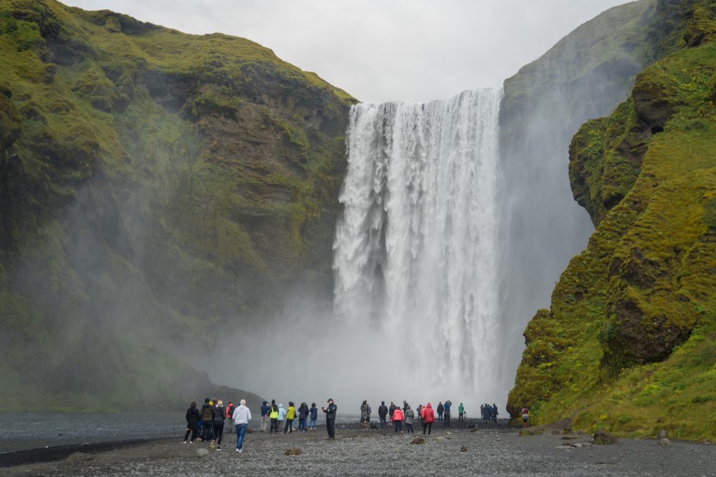 A few dozen people standing in front of a thick, tall waterfall.