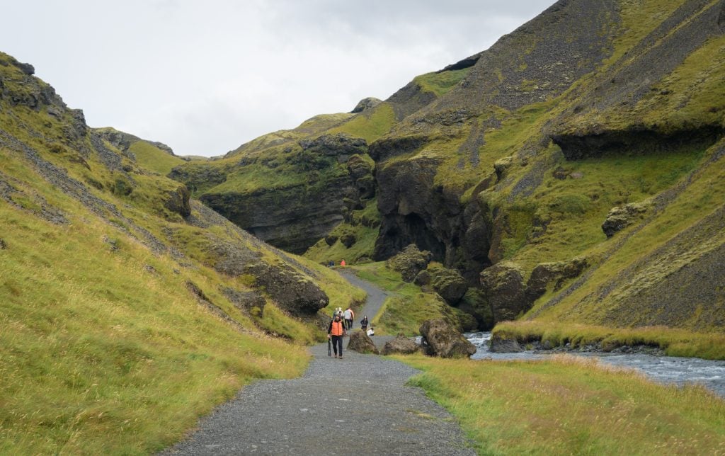 Hikers walking along a gravel path surrounded by green hills.