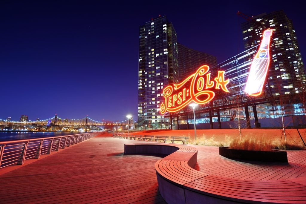 A Pepsi Cola neon light in front of sky scrapers